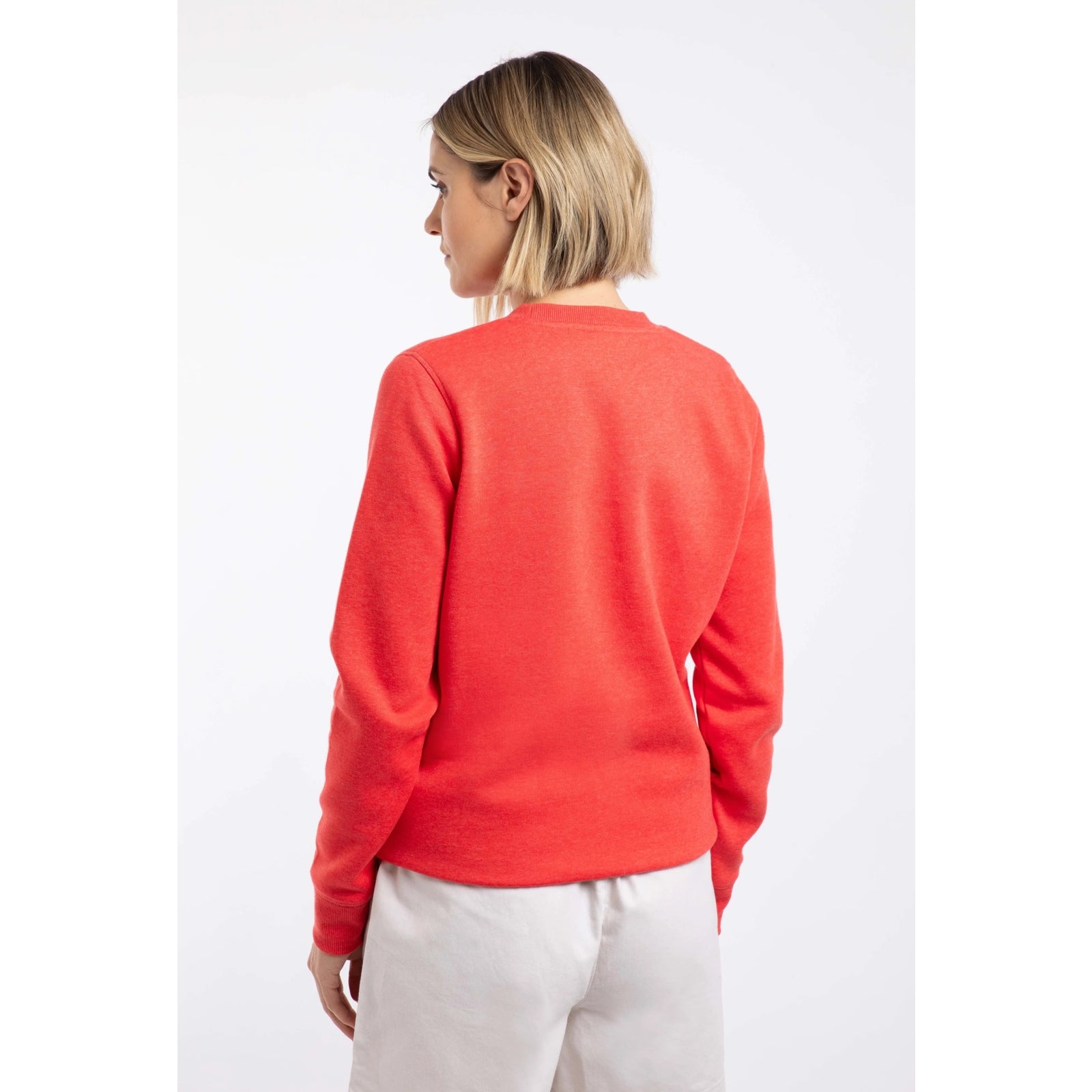 Back view of a woman wearing a Weird Fish Aurora crew neck sweatshirt in a bright coral colour with bold circular logo  print on the front.