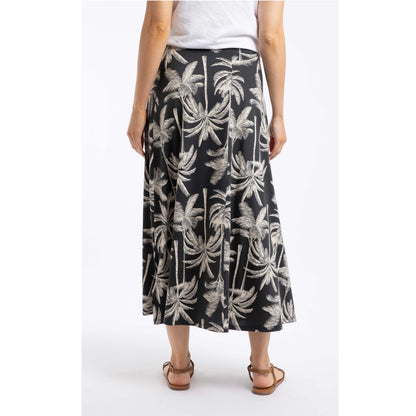 Back view of a woman wearing a Weird Fish Eloriah midi jersey skirt in black with a beige palm tree pattern.
