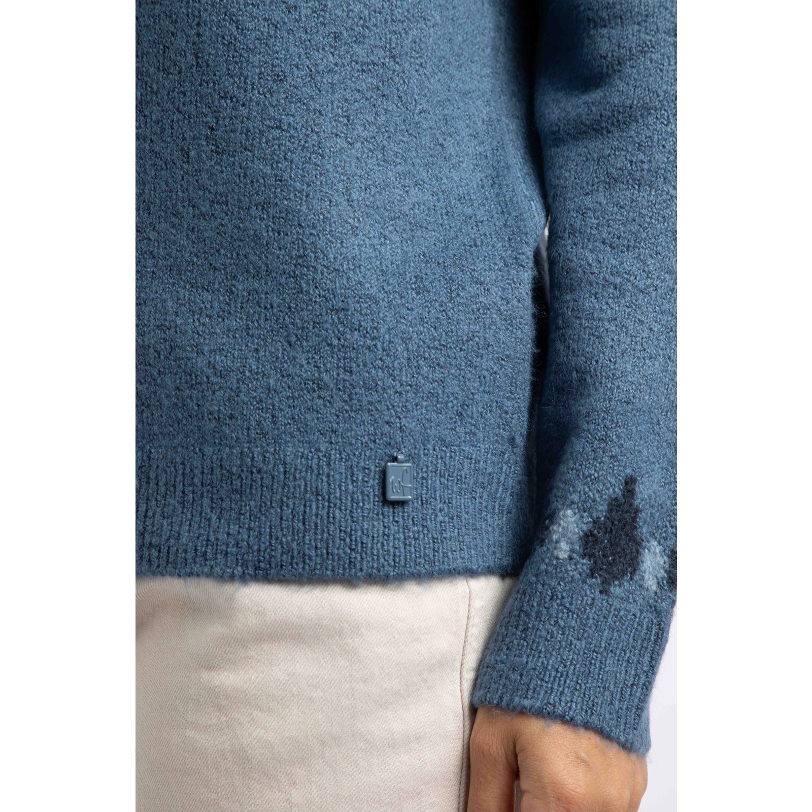 Close-up view of the sleeve cuff and small metal logo fob of a Weird Fish knitted Lowell jumper in Ash Blue, with a Fair Isle pattern across the chest and shoulders.