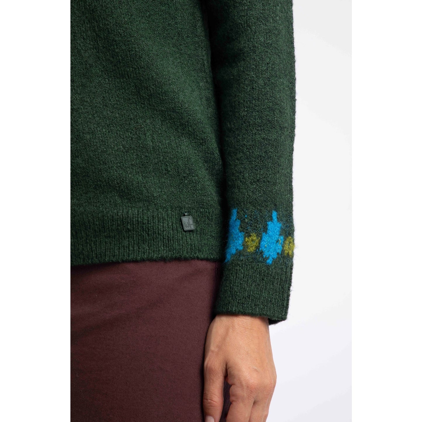 Close-up view of the sleeve cuff and small metal logo fob of a Weird Fish knitted Lowell jumper in Bottle Green, with a Fair Isle pattern across the chest and shoulders.