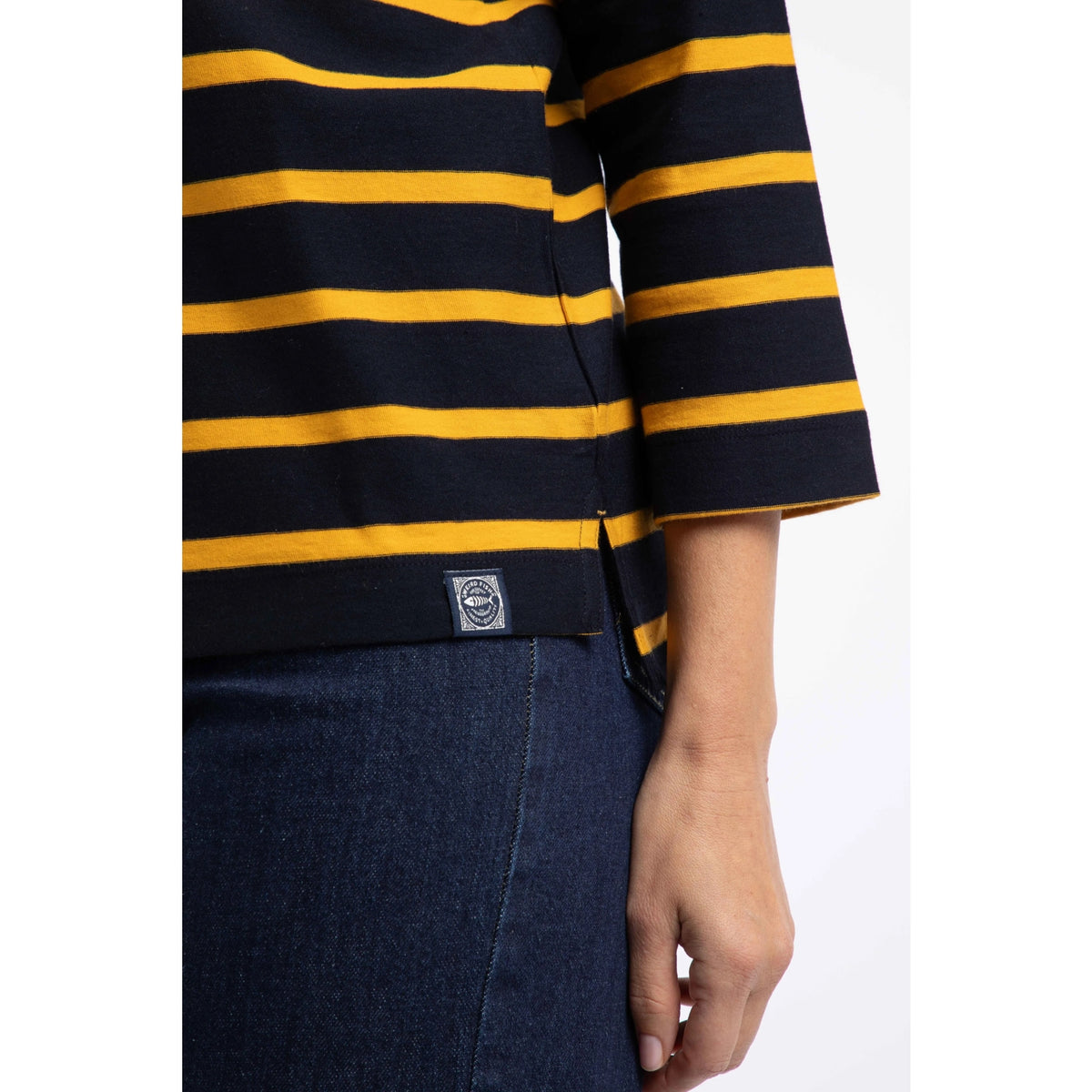Close-up view of the logo hem on a womens Weird Fish Saffira 3/4 length sleeve top in Midnight Navy with Gold Yellow stripes.