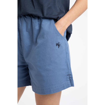 Close-up view of a woman wearing a pair of Weird Fish Jardin elastic waist twill cotton shorts in Faded Blue with hip pockets and small embroidered logo.