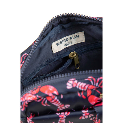 Close-up view of the zip top and internal pocket of a Weird Fish Corrie small cross body bag, in Mid Navy with a red lobster pattern.