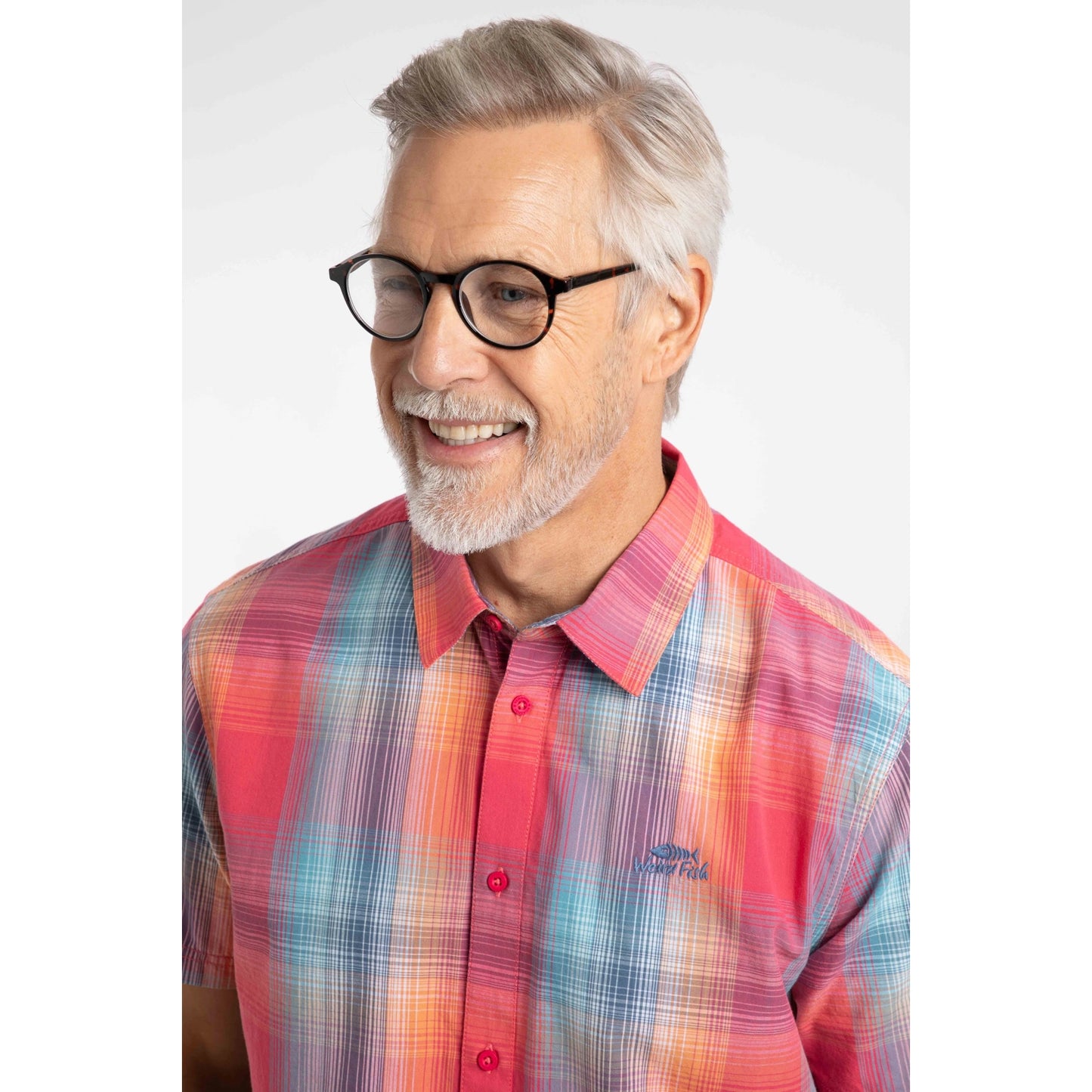 Close-up view of a man wearing a Weird Fish short sleeve Judd shirt in a bright Flamingo Pink, blue and orange check pattern with blue jeans.