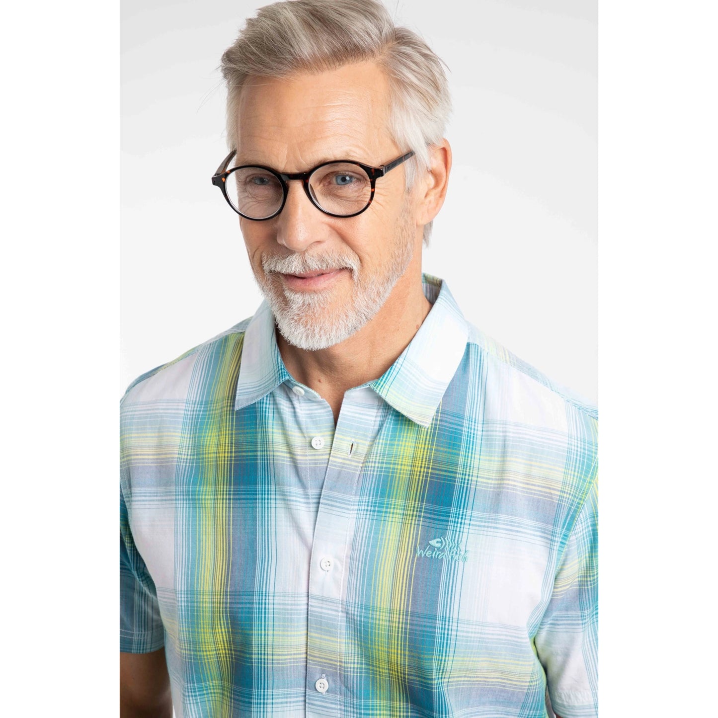 Close-up view of a man wearing a Weird Fish short sleeve Judd shirt in an off white, blue and lime green check pattern.