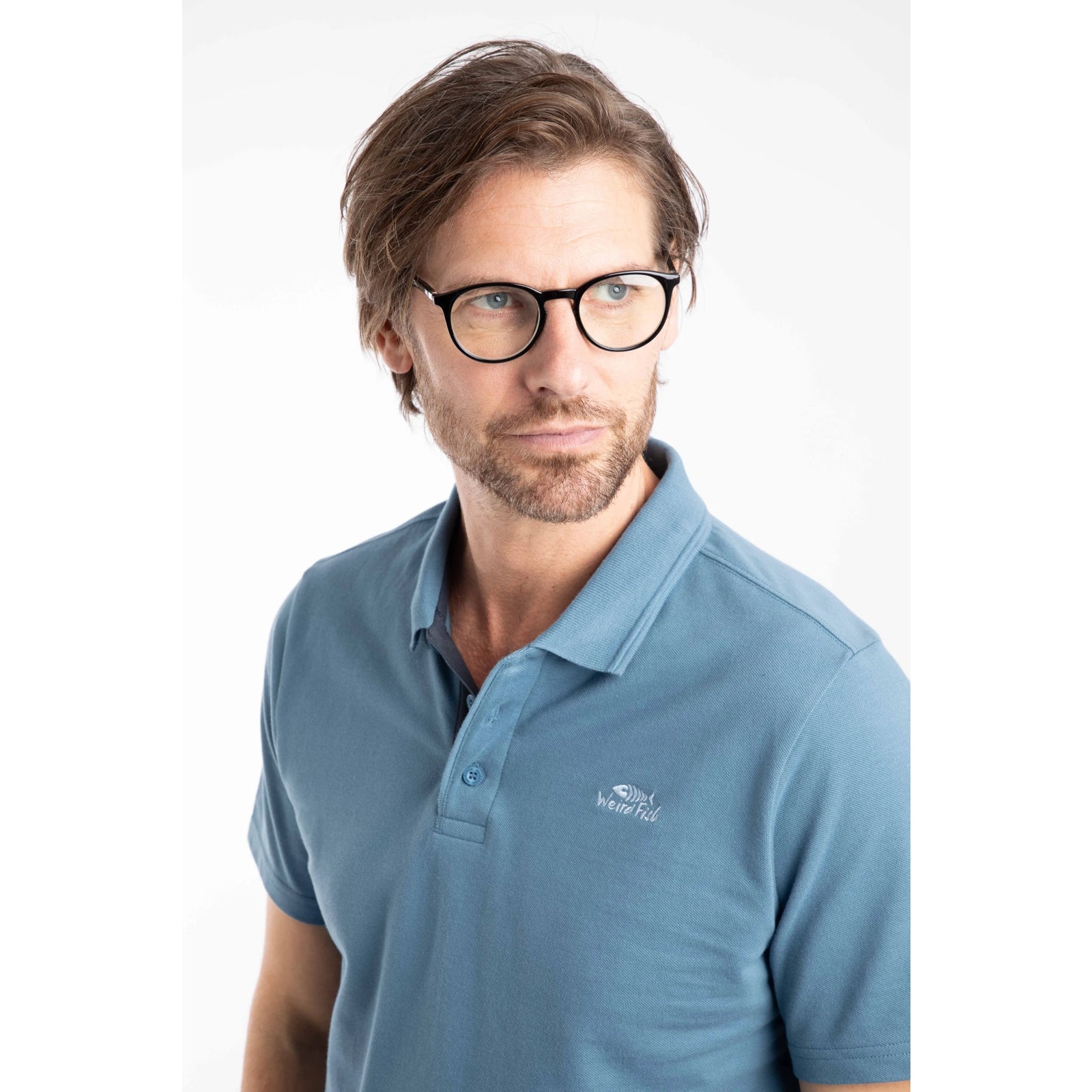 Close-up view of a man wearing a short sleeve Weird Fish Miles pique polo shirt in Faded Blue.