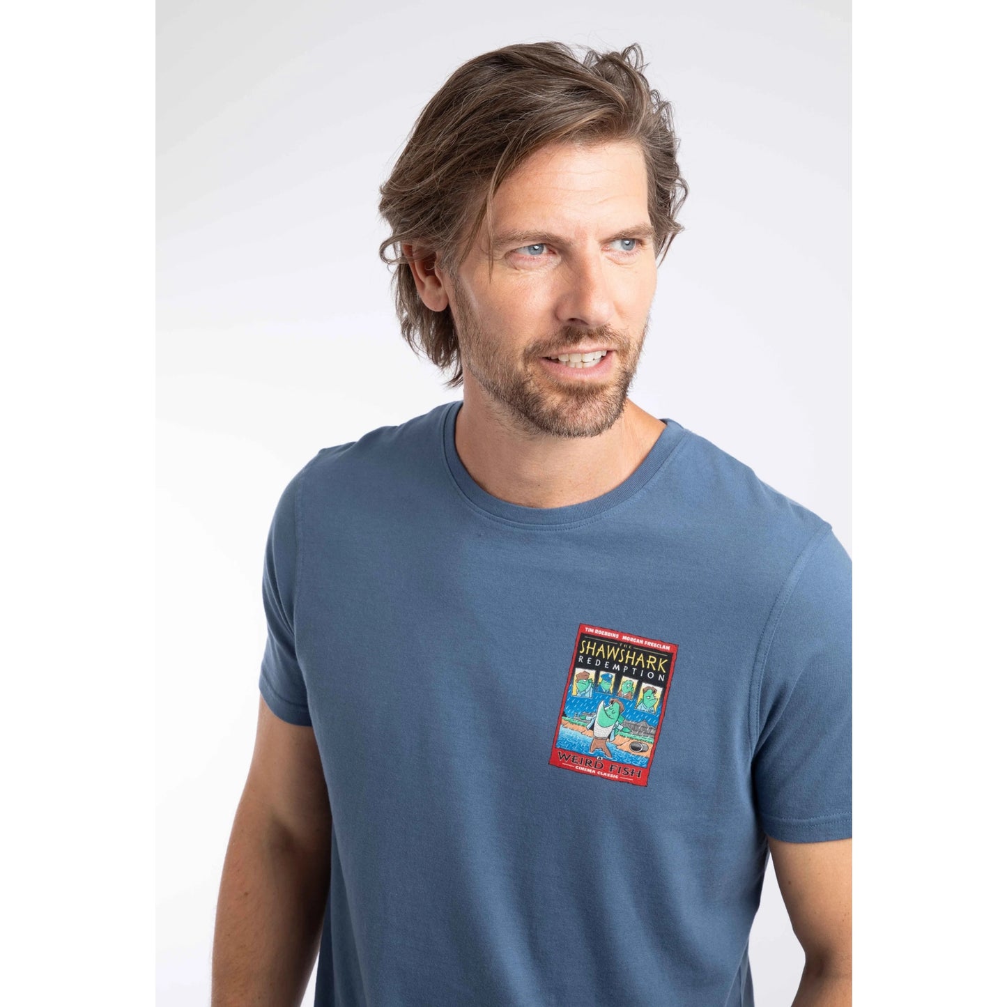 Close-up view of a man wearing a short sleeve t-shirt in Ensign Blue, featuring a small Shawshark Redemption parody print of The Shawshank Redemption film poster on one side of the chest.