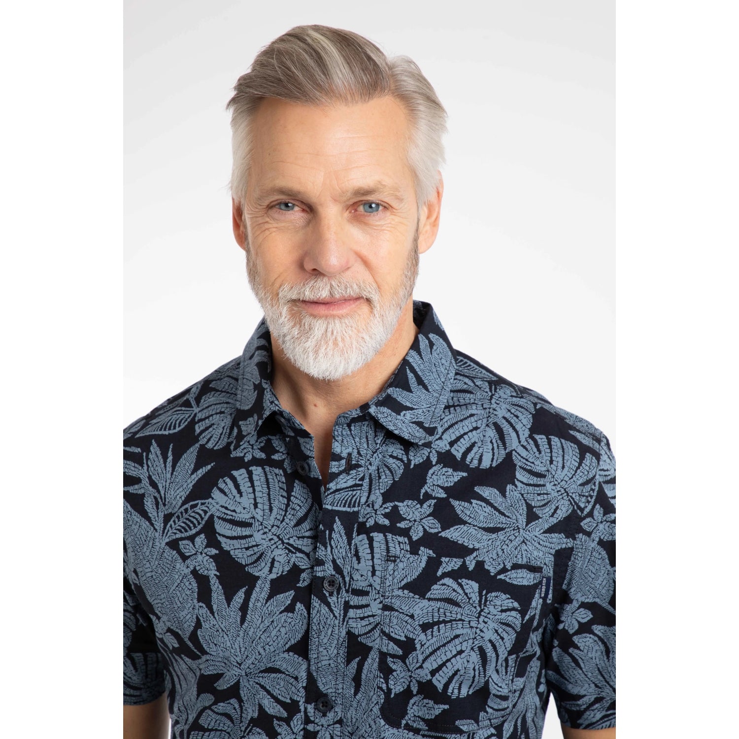 Close-up view of a man wearing a Weird Fish short sleeve Faraway shirt in Blue Mirage with a tropical leaf pattern