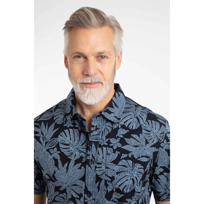 Close-up view of a man wearing a Weird Fish short sleeve Faraway shirt in Blue Mirage with a tropical leaf pattern