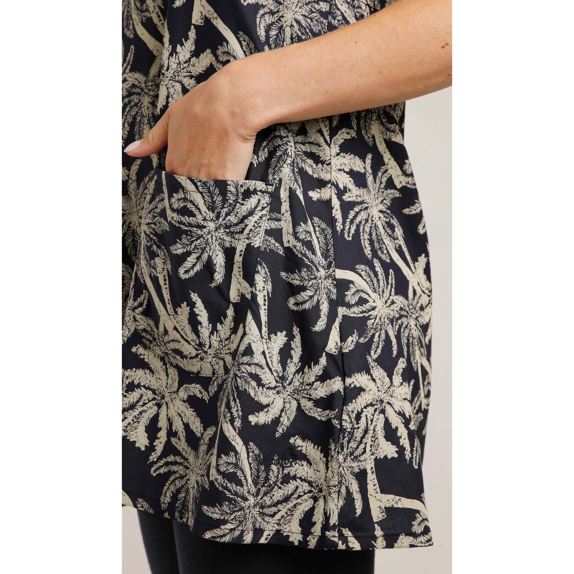 Close-up view of a pocket on the front of a woman wearing a Weird Fish short sleeve Breeza tunic in Midnight Navy with a beige palm tree pattern.