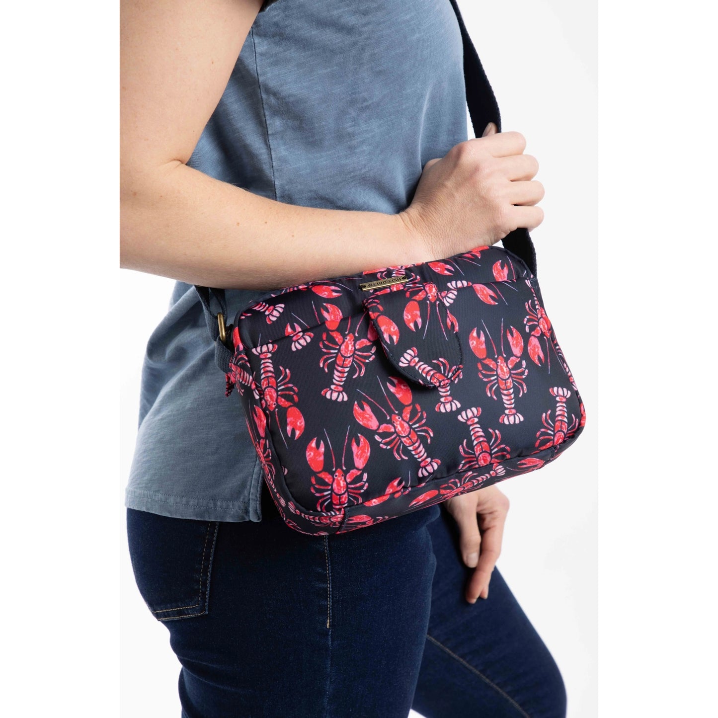 Woman holding a Weird Fish Corrie small cross body bag, in Mid Navy with a red lobster pattern and adjustable shoulder strap.