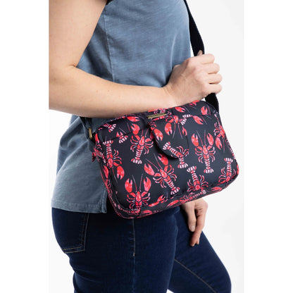 Woman holding a Weird Fish Corrie small cross body bag, in Mid Navy with a red lobster pattern and adjustable shoulder strap.