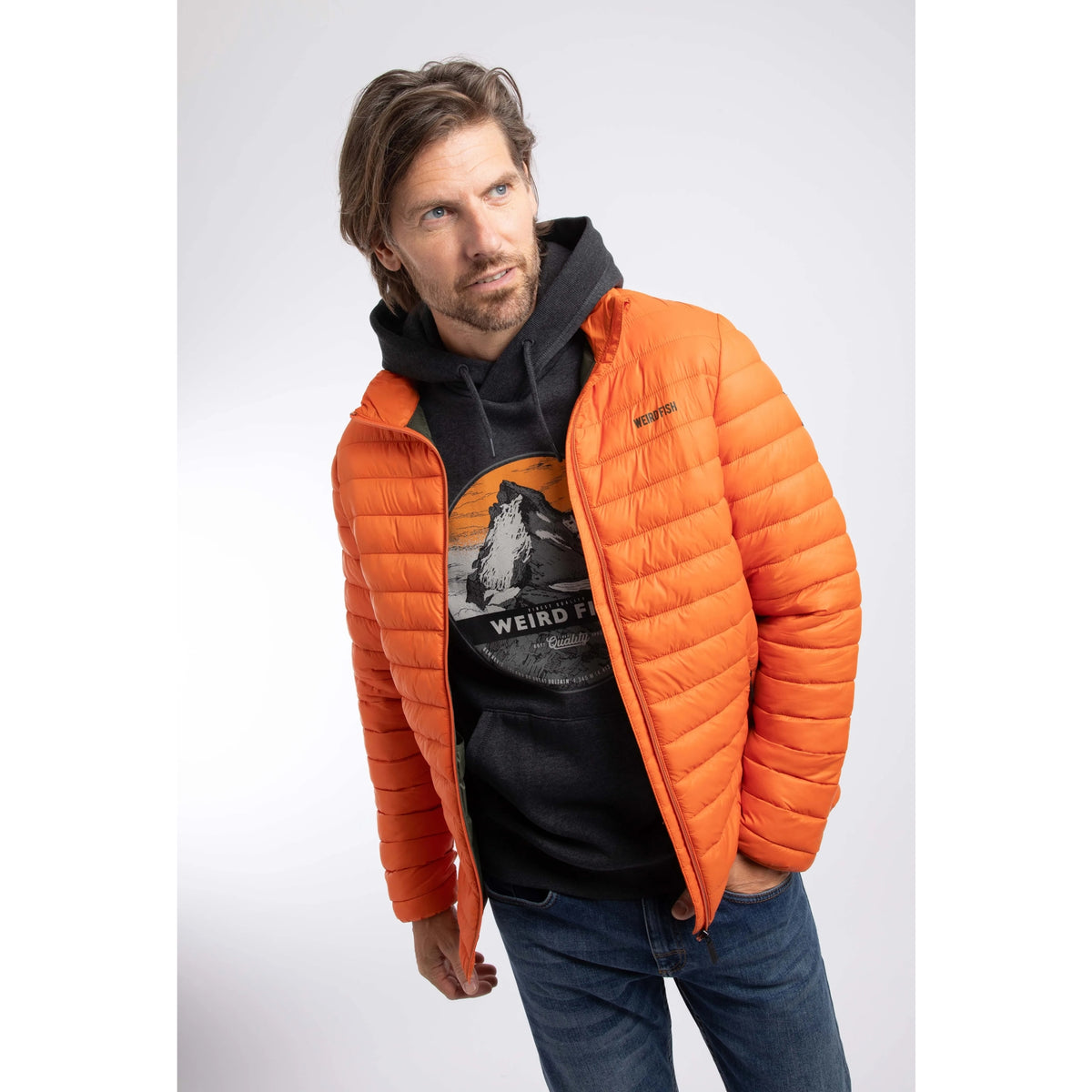 A man wearing a Weird Fish Crantock padded lightweight showerproof jacket in bright Koi Orange.