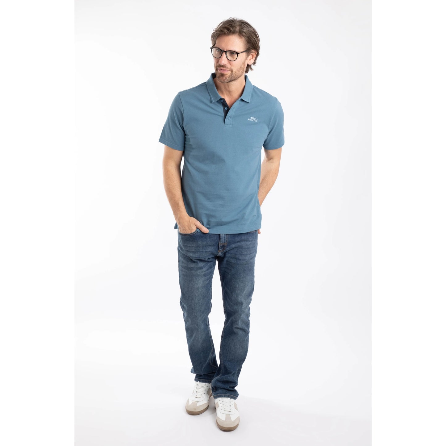 Man wearing a short sleeve Weird Fish Miles pique polo shirt in Faded Blue, with blue jeans and white trainers.
