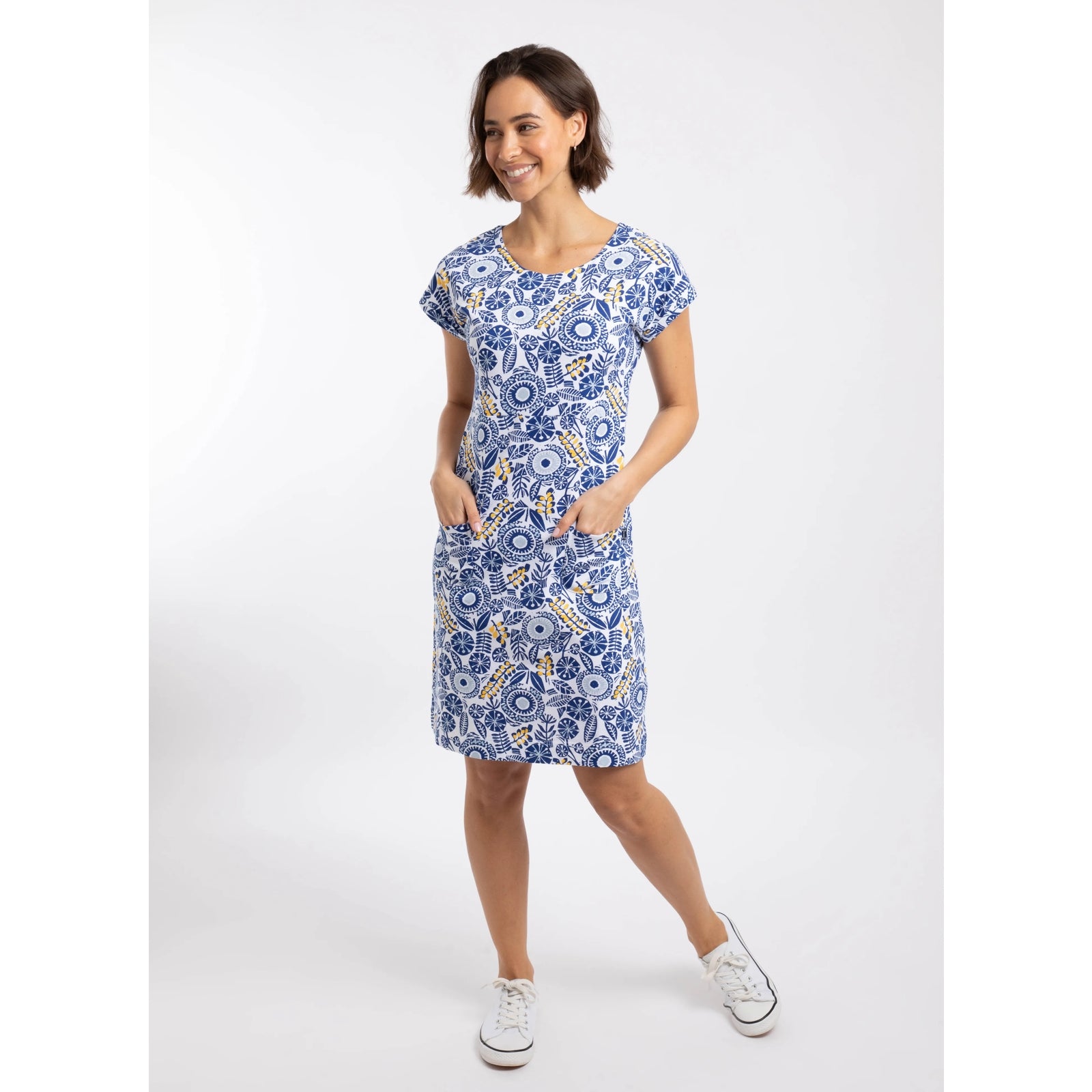 A woman wearing a Weird Fish short sleeve Tallahassee dress in Sapphire Blue featuring an abstract floral print with front pockets and white trainers.
