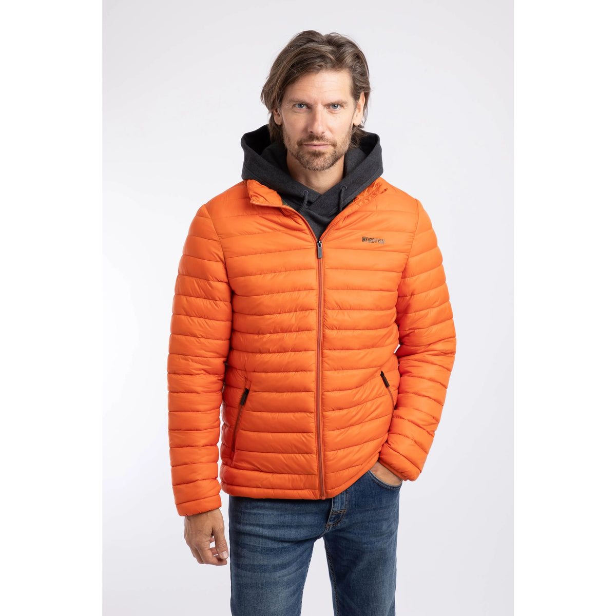 Front view of a man wearing a Weird Fish Crantock padded lightweight showerproof jacket in bright Koi Orange.