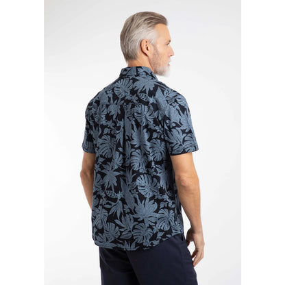Back view of a man wearing a Weird Fish short sleeve Faraway shirt in Blue Mirage with a tropical leaf pattern