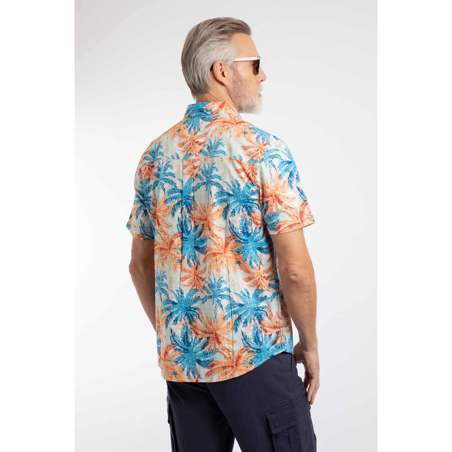 Back view of a man wearing a Weird Fish short sleeve Faraway shirt in Paprika orange and blue with a tropical palm tree pattern and navy shorts