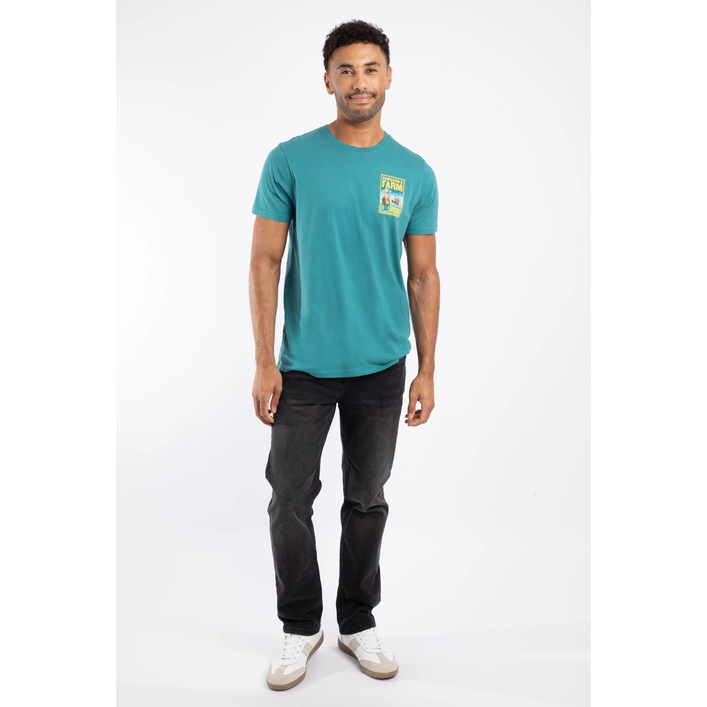 Man wearing a Weird Fish teal t-shirt with a Barksons Farm print on a white background