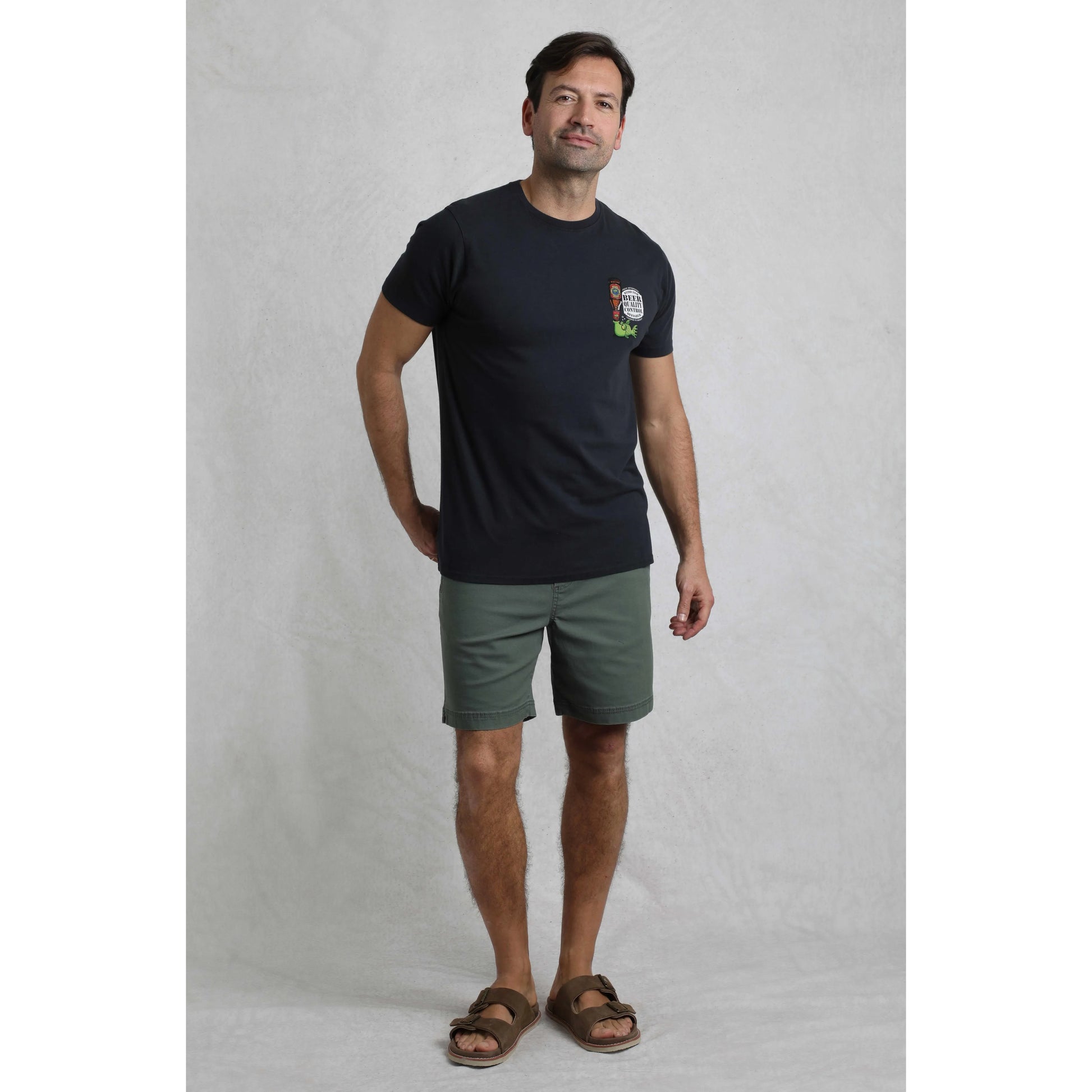 Man wearing a black t-shirt with a logo and green shorts on a grey background