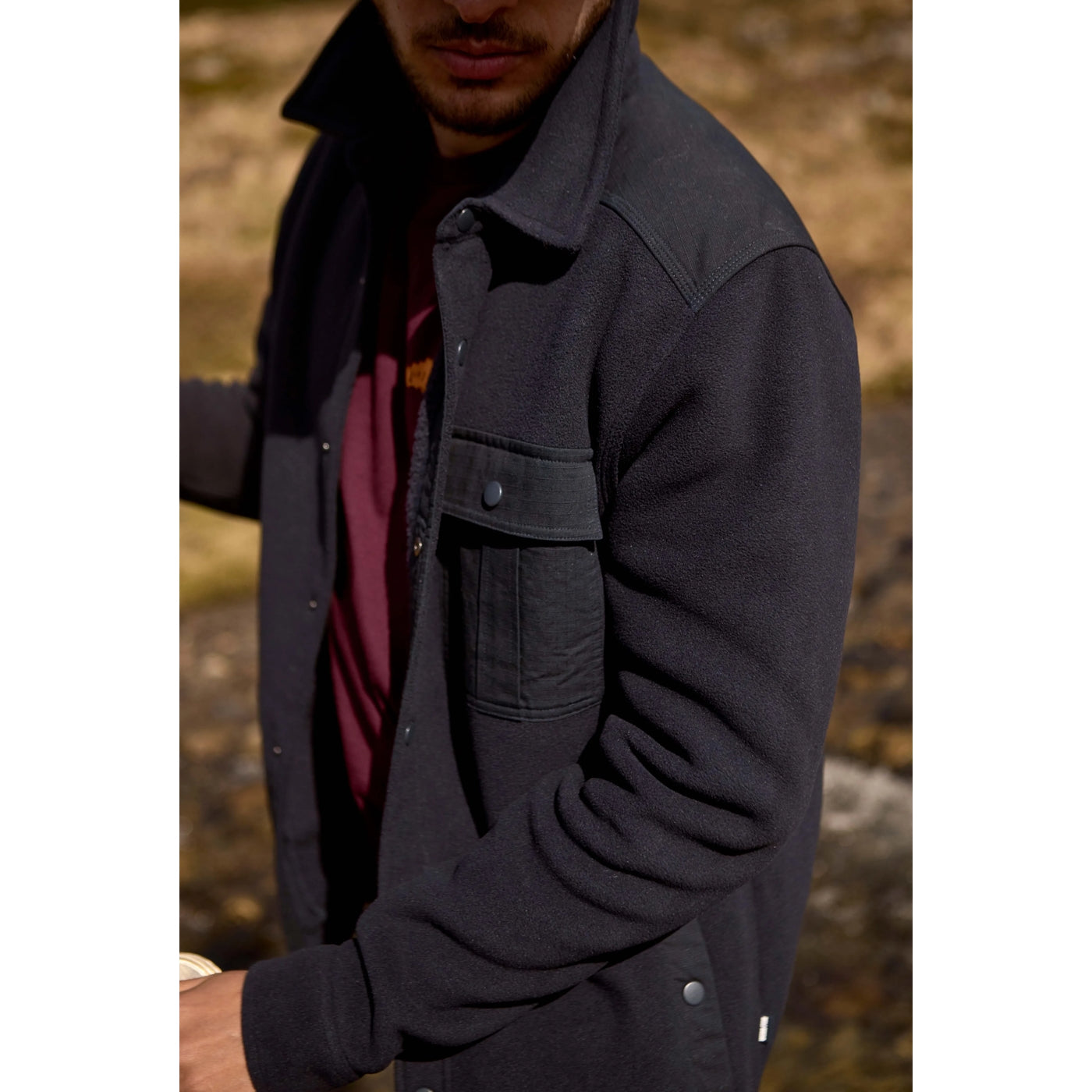 Man wearing a Weird Fish dark navy Boyd fleece jacket with a blurred natural background