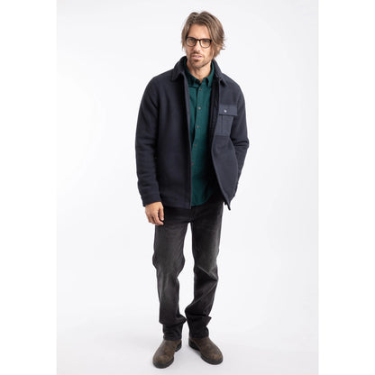 Man wearing a dark navy Weird Fish Boyd fleece jacket, green shirt, and grey pants on a white background