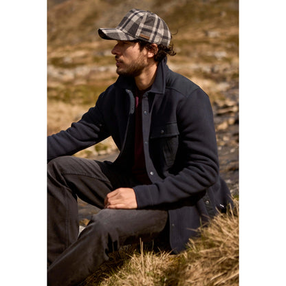 Man wearing a dark navy Weird Fish Boyd fleece jacket and plaid cap sitting in a natural setting