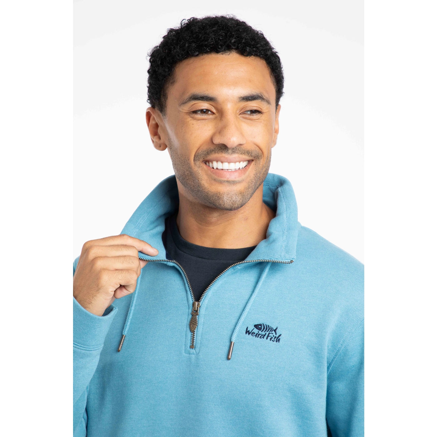 Man wearing a sky blue Weird Fish sweatshirt with a logo on a white background