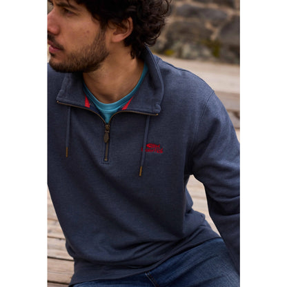 Man wearing a navy blue Weird Fish Brampton pullover sweatshirt with a red logo, sitting outdoors.