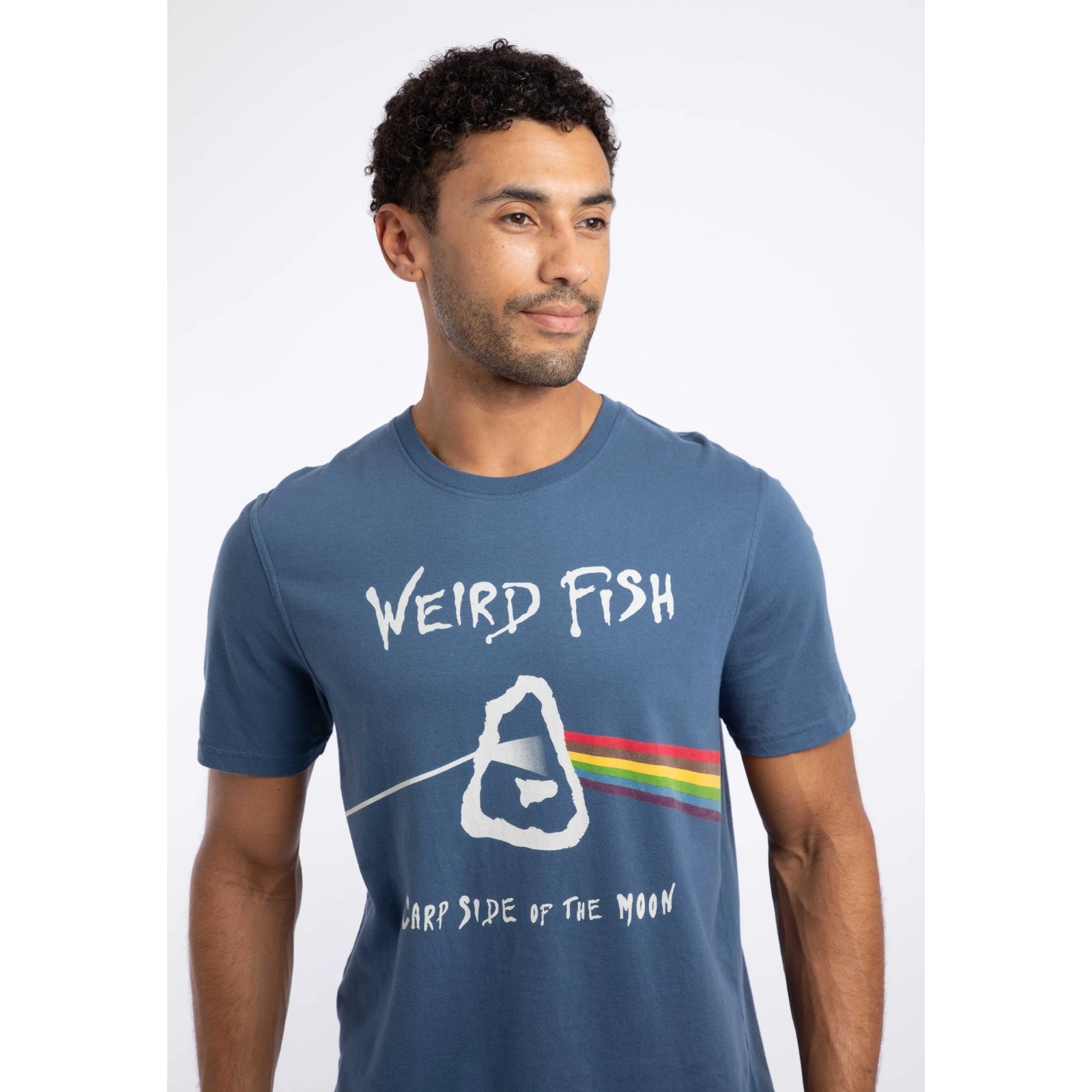 Close-up view of a man wearing a Weird Fish 'Carp Side of the Moon' printed short sleeve t-shirt in Ensign Blue, featuring a Pink Floyd themed graphic print, with the text 'WEIRD FISH' and 'CARP SIDE OF THE MOON'.