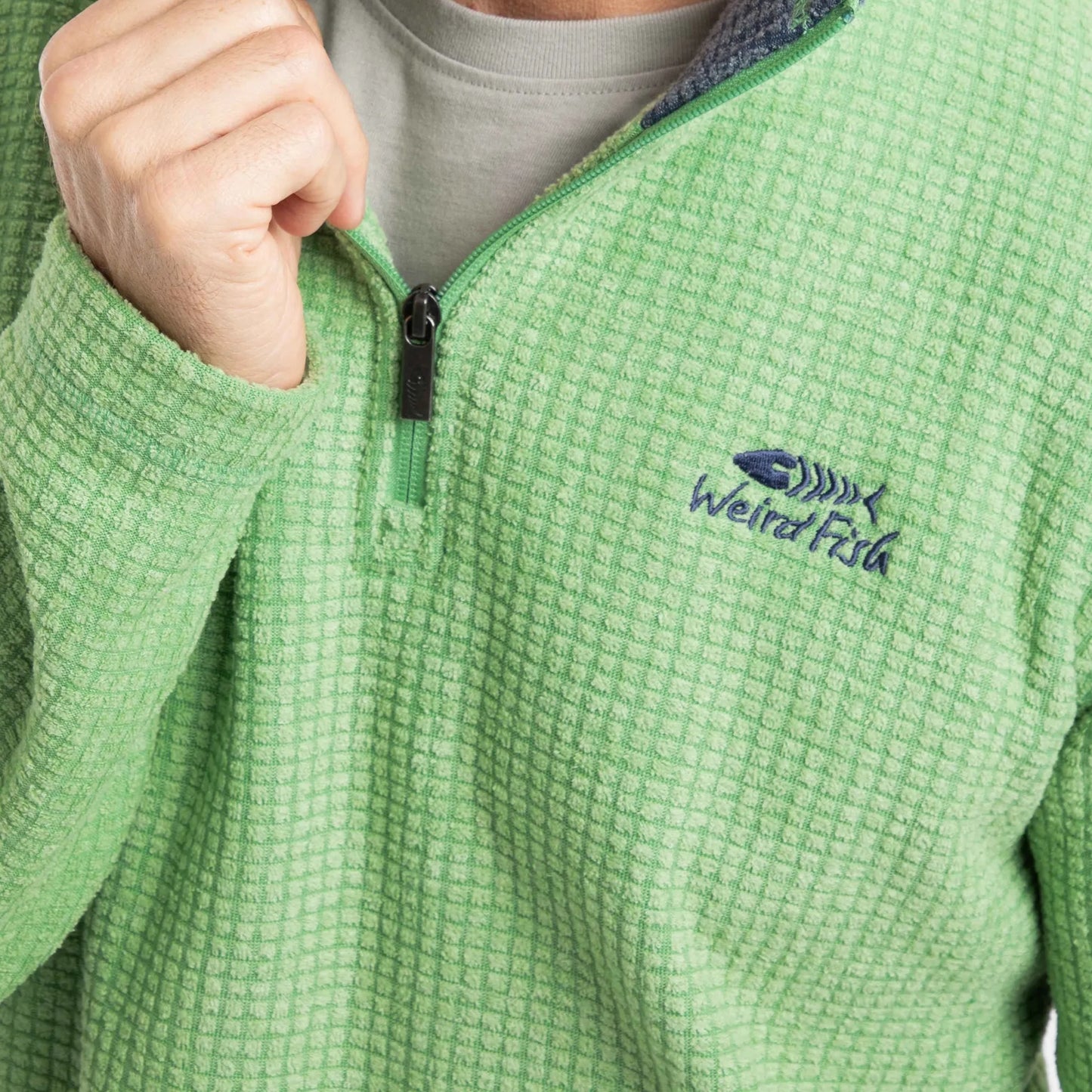 Close-up view of the 1/4 zip neckline and chest logo of a mens Weird Fish Newark grid fleece in grass green