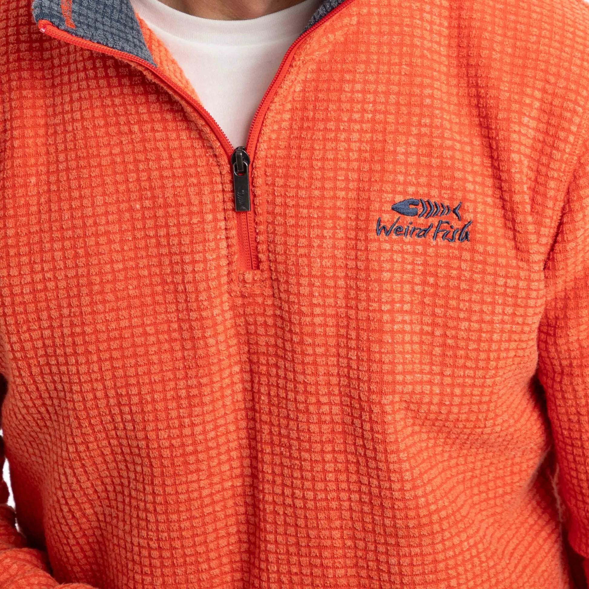 Close-up view of the 1/4 zip neckline and chest logo of a mens Weird Fish Newark grid fleece in Orange Spice