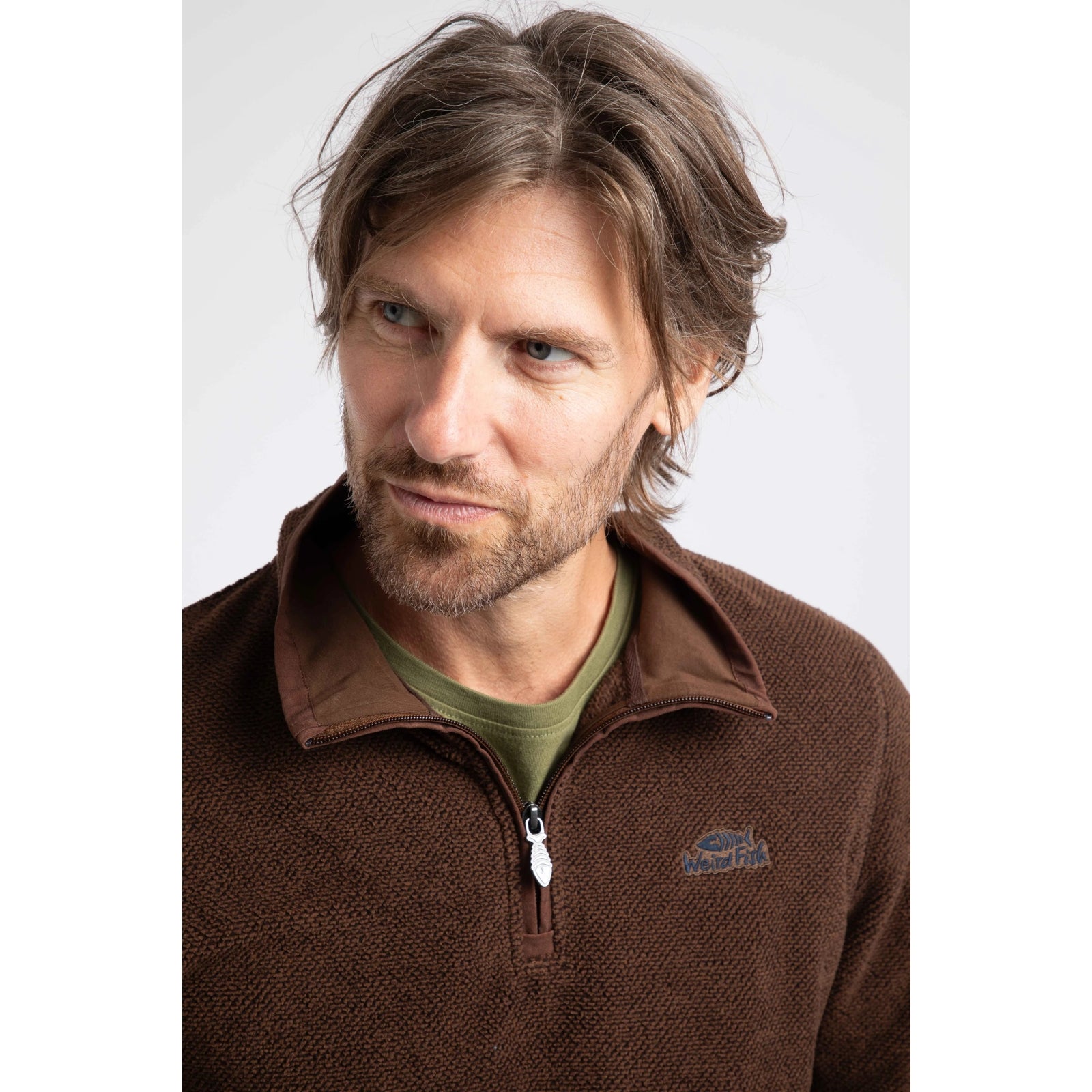 Close-up view of a man wearing a Weird Fish quarter zip textured Errill fleece in Chocolate brown with a small logo on one side of the chest.