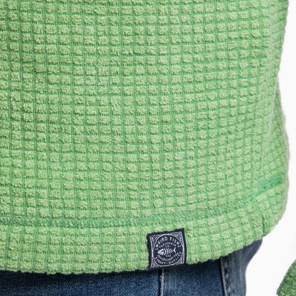 Close-up view of a logo label on the hem of a mens Weird Fish Newark grid fleece in grass green