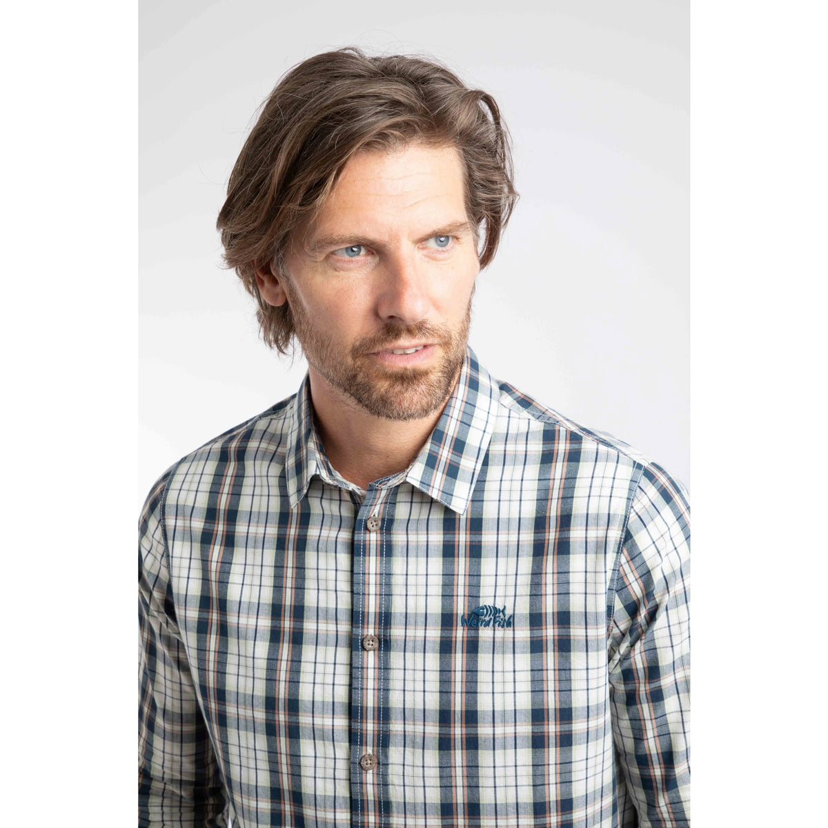 Close-up view of a man wearing a Weird Fish long sleeve Lando shirt, in Off White with a navy, green and orange check pattern.