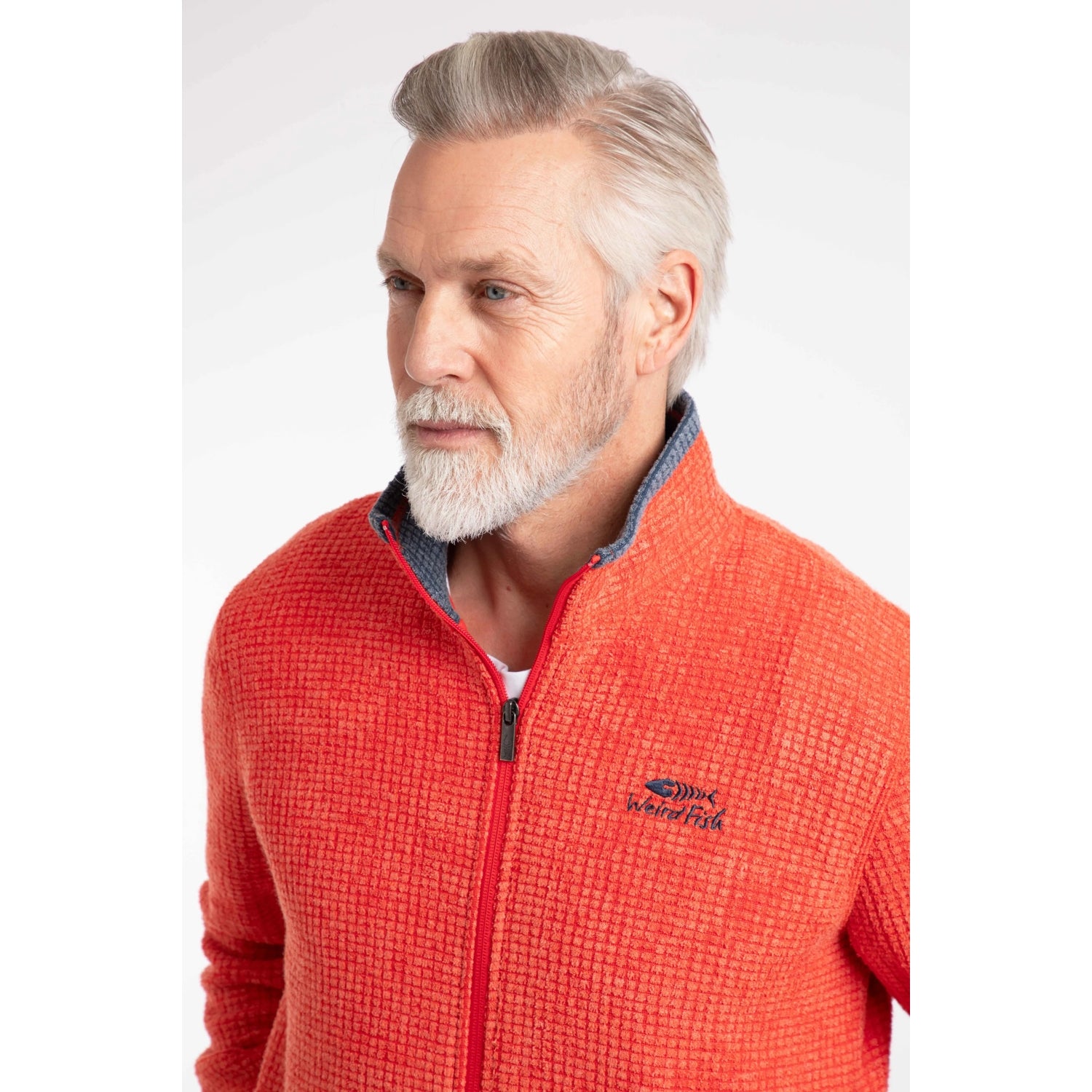 Close-up view of a man wearing a Weird Fish full zip Shires grid textured fleece in bright Orange Spice with contrasting navy neckline and small chest logo