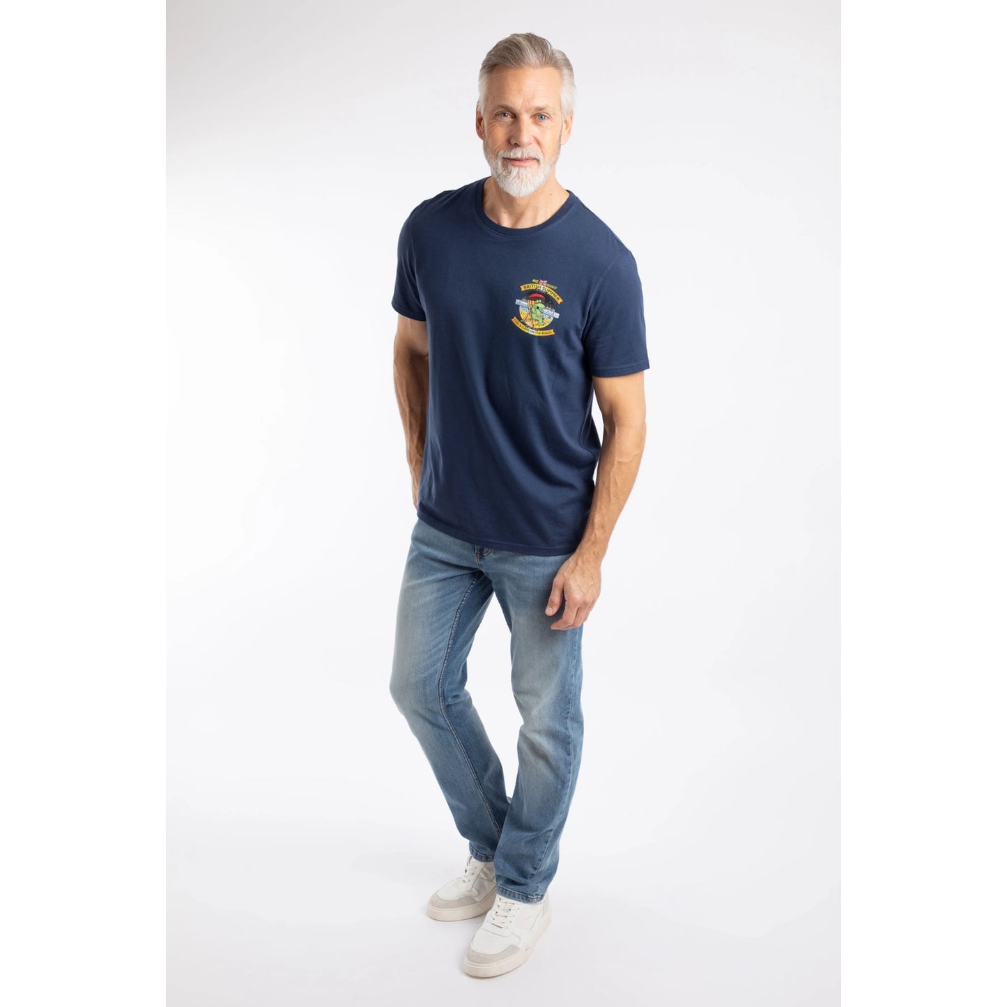 A man wearing a Weird Fish Cod and Chips print short sleeve t-shirt in Dark Blue with blue jeans and white shoes