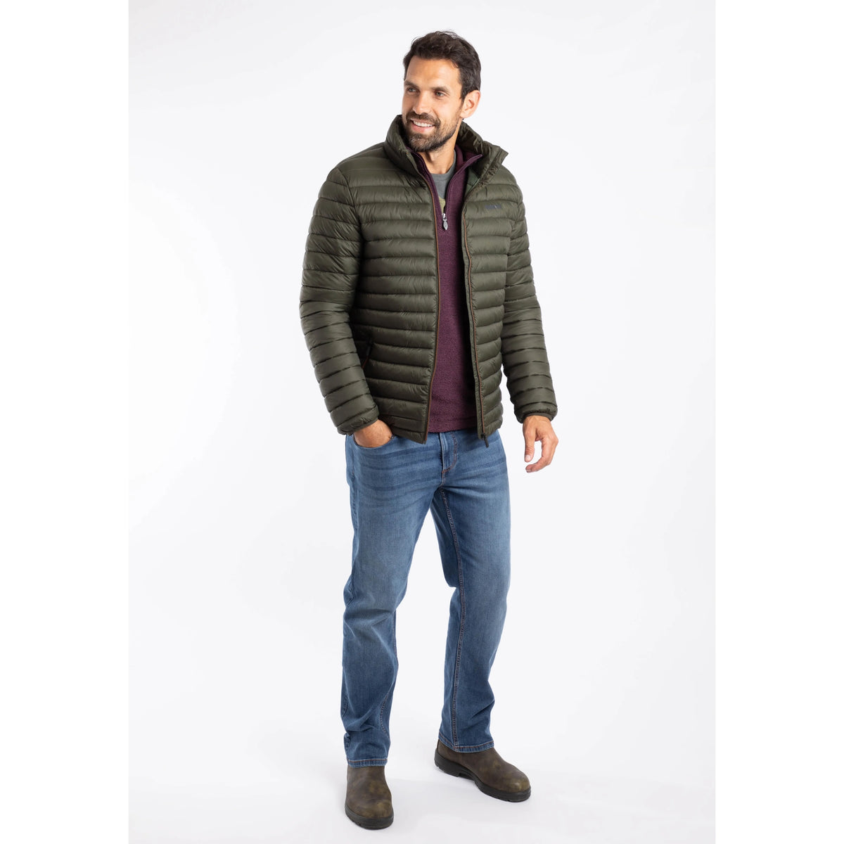 A man wearing a Weird Fish Crantock padded showerproof jacket in Anthracite  with blue jeans and brown boots