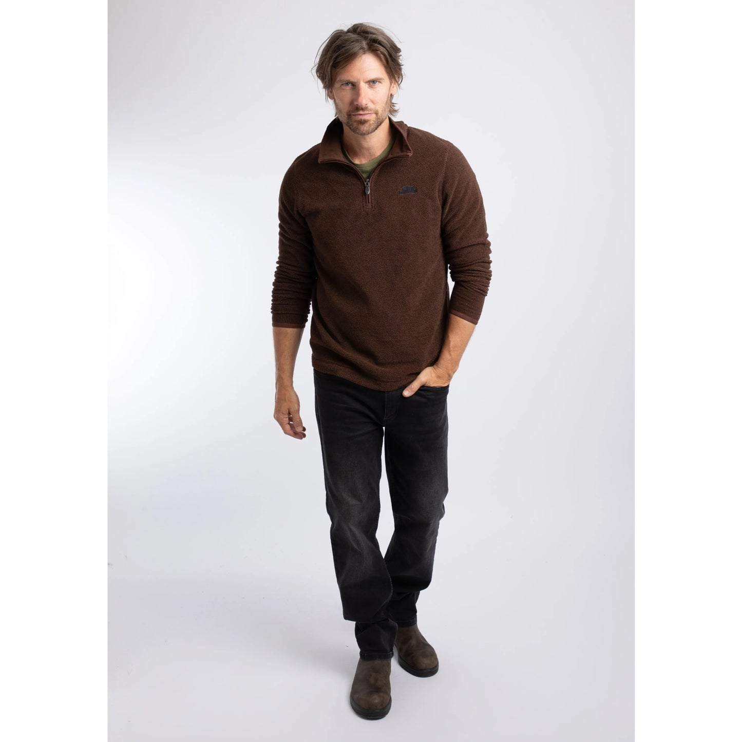 A man wearing a Weird Fish quarter zip textured Errill fleece in Chocolate brown with black trousers and boots.