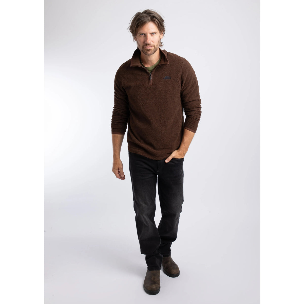 A man wearing a Weird Fish quarter zip textured Errill fleece in Chocolate brown with black trousers and boots.