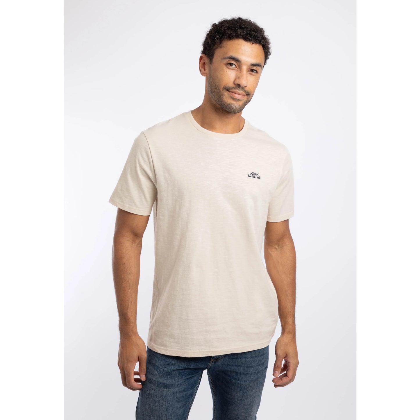 Front view of a man wearing a Weird Fish crew neck short sleeve Fished t-shirt in Egg Shell with small logo on one side of the chest.