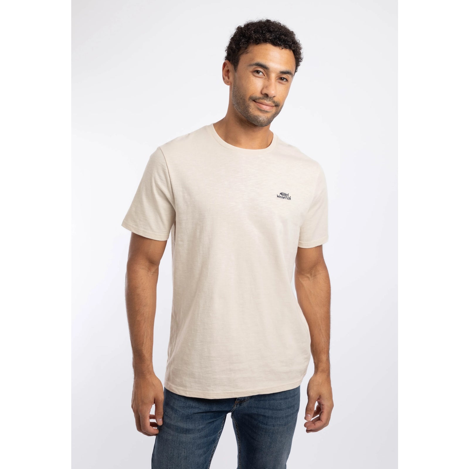 Front view of a man wearing a Weird Fish crew neck short sleeve Fished t-shirt in Egg Shell with small logo on one side of the chest.