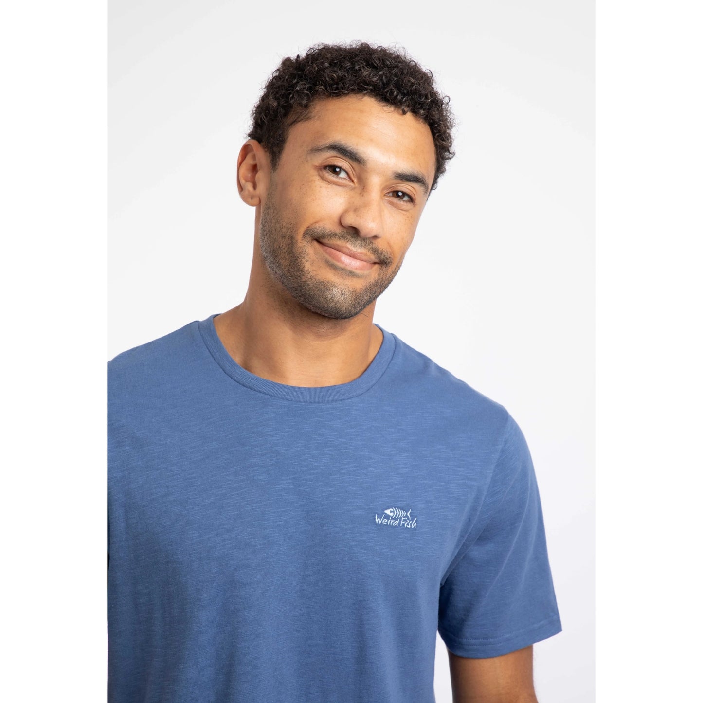 Close-up view of a man wearing a Weird Fish short sleeve Fished t-shirt in Faded Blue with a small logo on the chest.