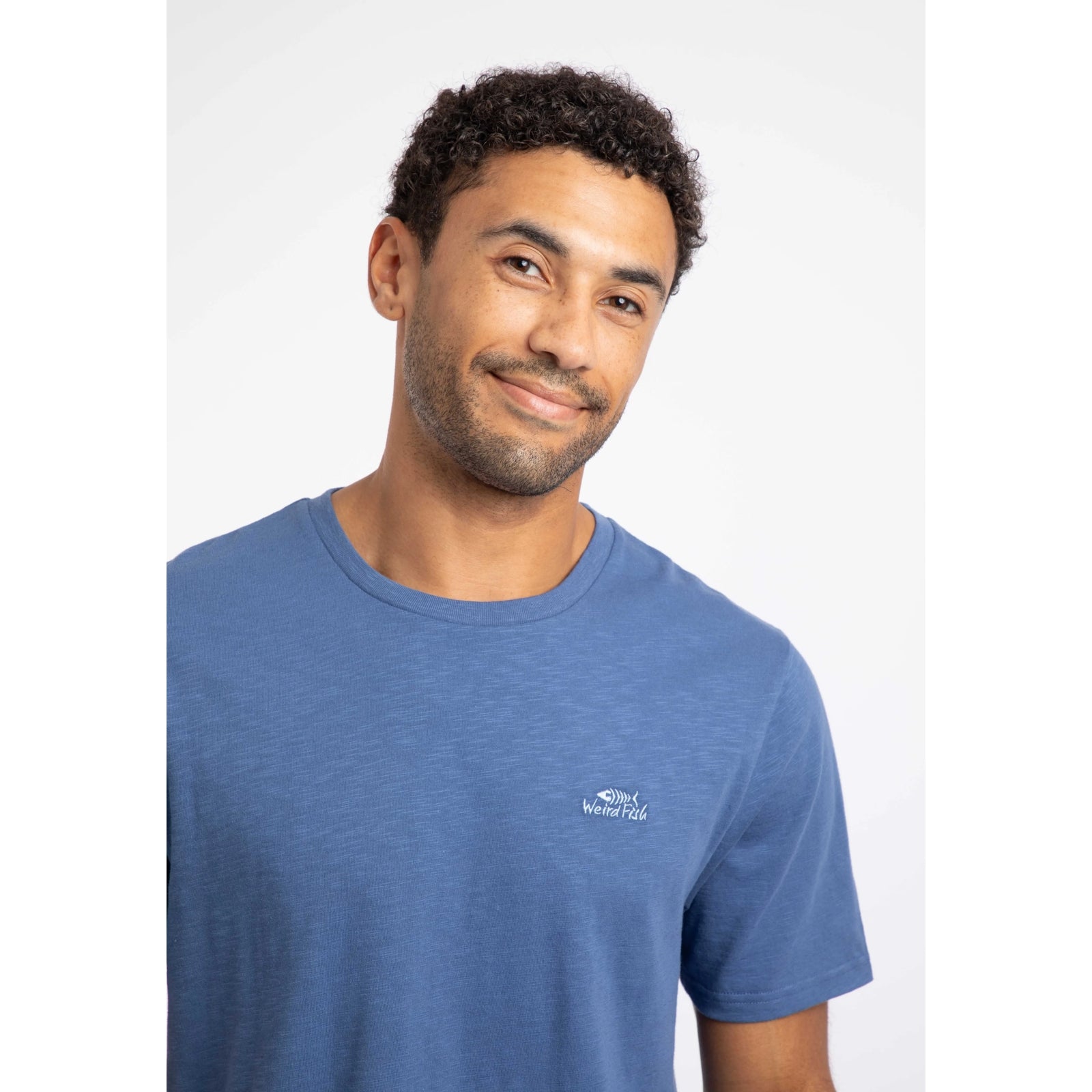 Close-up view of a man wearing a Weird Fish short sleeve Fished t-shirt in Faded Blue with a small logo on the chest.