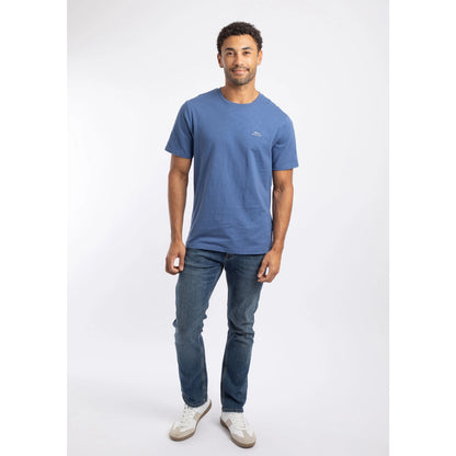 Man wearing a Weird Fish short sleeve Fished t-shirt in Faded Blue with a small logo on the chest, with blue jeans and white trainers.