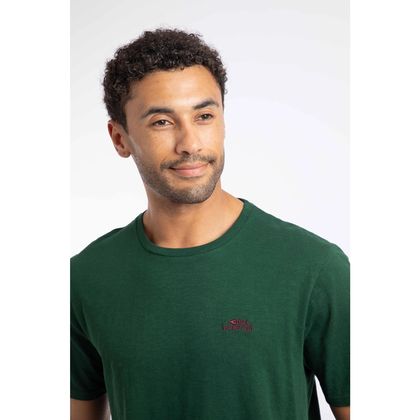 Close-up view of a man wearing a Weird Fish short sleeve Fished t-shirt in Pine Green, plain with a small logo on the chest