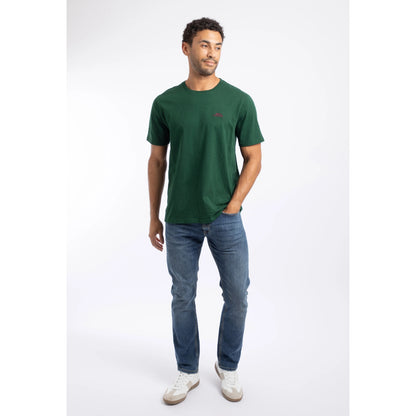 A man wearing a Weird Fish short sleeve Fished t-shirt in Pine Green, with blue jeans and white trainers.