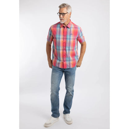 A man wearing a Weird Fish short sleeve Judd shirt in a bright Flamingo Pink, blue and orange check pattern with blue jeans and white trainers.