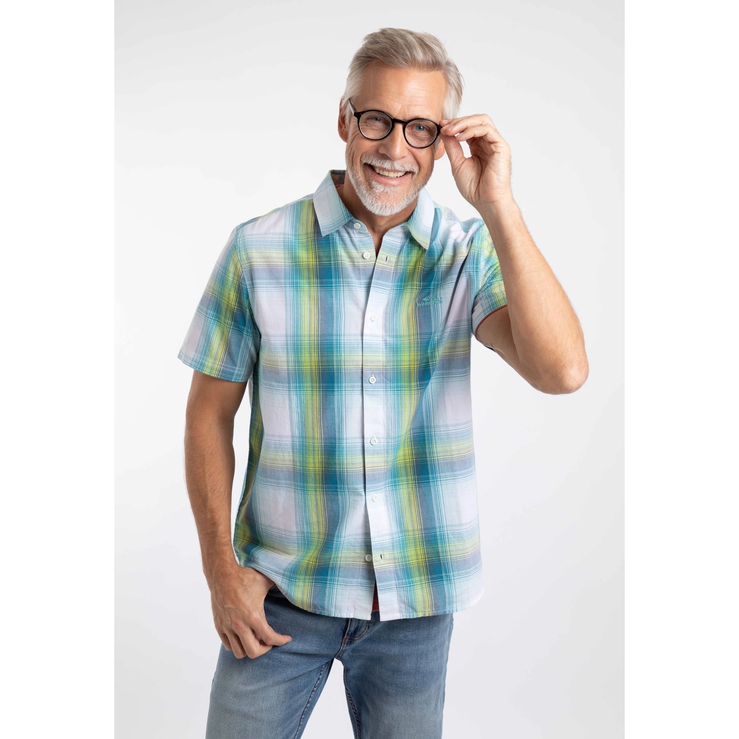 A man wearing a Weird Fish short sleeve Judd shirt in an off white, blue and lime green check pattern with blue jeans.