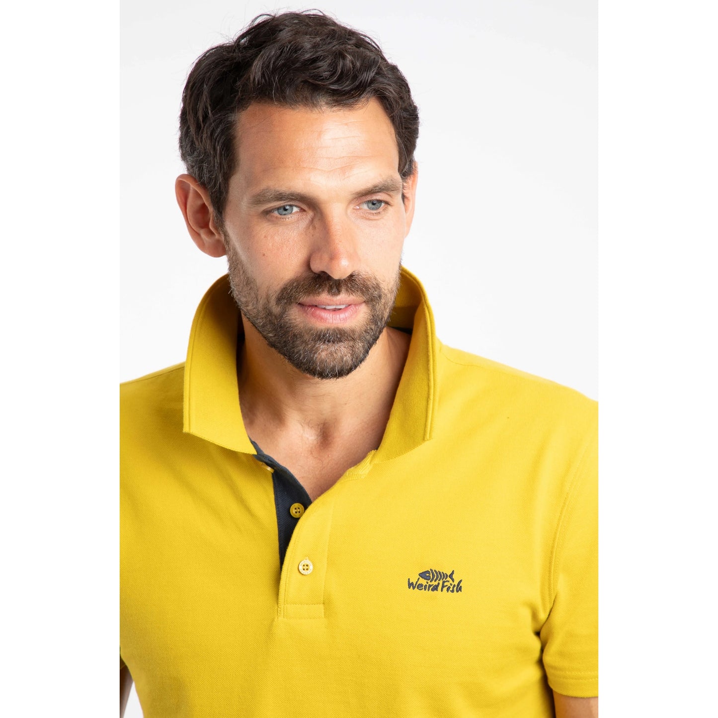 Man wearing a Weird Fish Miles Antique Moss yellow polo shirt with a logo on a white background